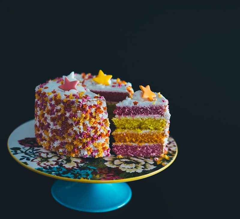 Rainbow layer cake covered in sprinkles, sliced to show colourful layers