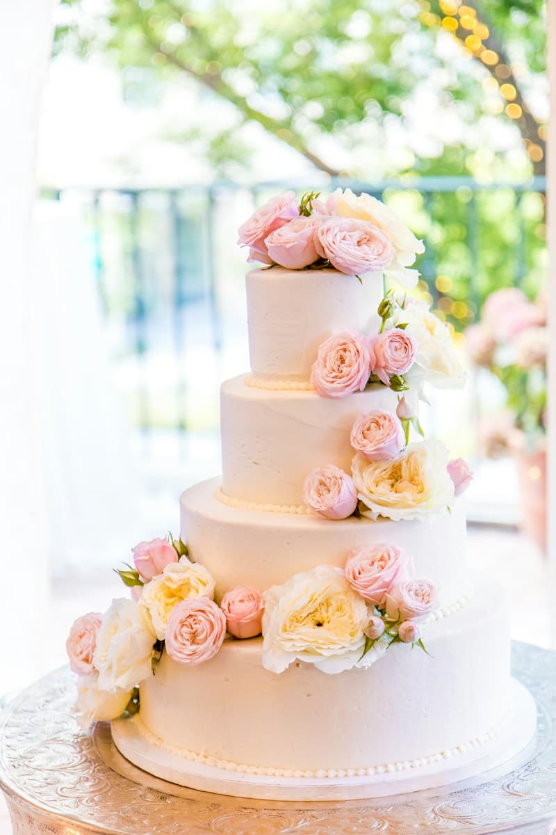 Four-tier white wedding cake decorated with pink roses